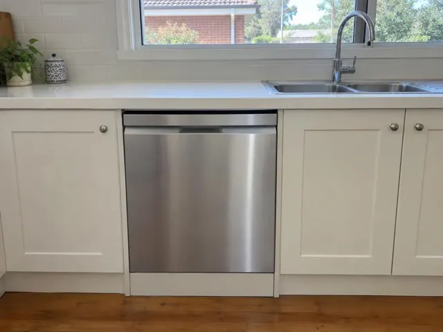 Built-in dishwasher below a kitchen benchtop beside a sink and cream cabinets in Weston