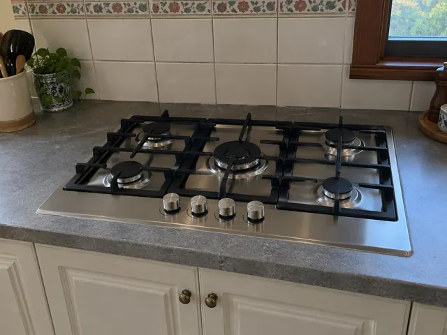 Stainless gas cooktop set into a grey benchtop with tiled splashback and window in Cessnock