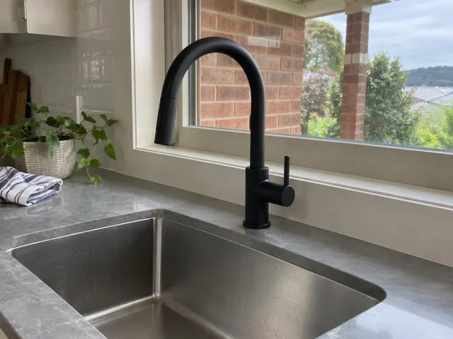 Black kitchen mixer tap beside a stainless sink and window over a stone benchtop in Abermain